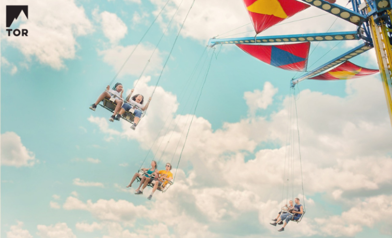 low angle photograph of a carnival tiltawhirl swingset with people swinging next to soft white clouds